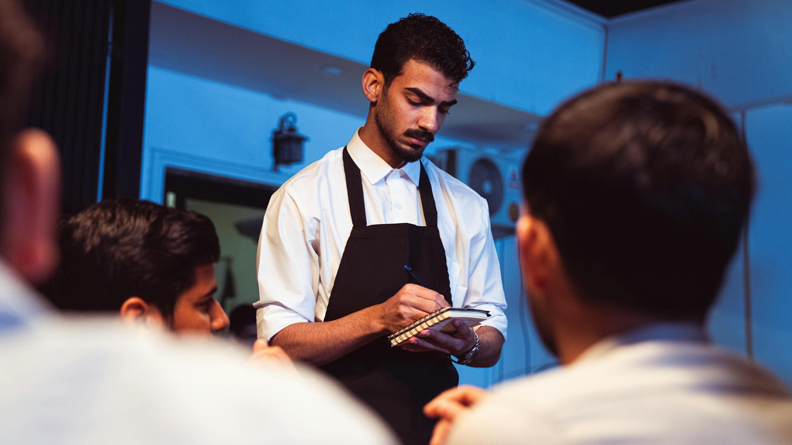 Attentive waiter writing down a customer's order in a cozy indoor restaurant.
