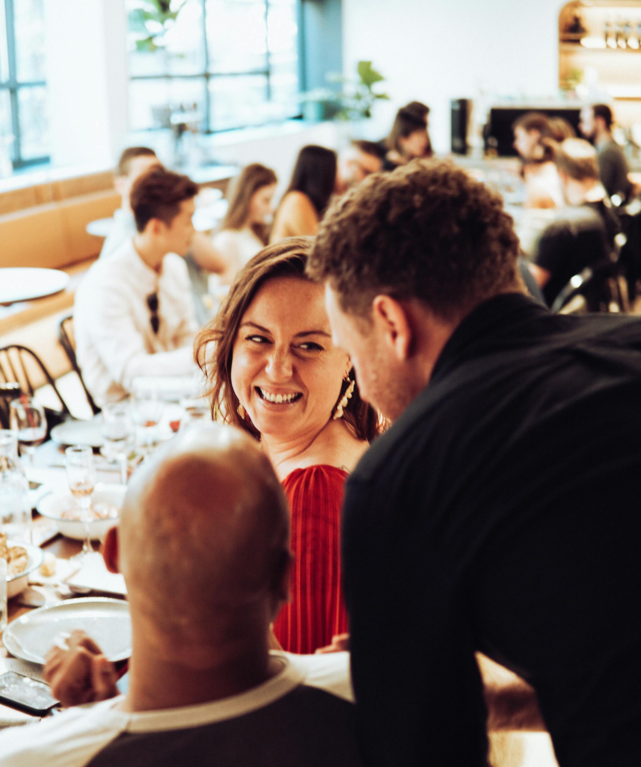 Group of friends enjoying lively conversation and dining in a restaurant setting.